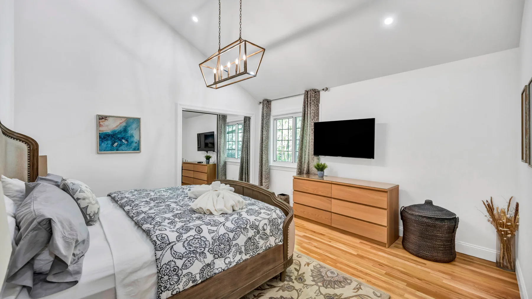 A bright bedroom with a patterned bedspread and a television on the wall.