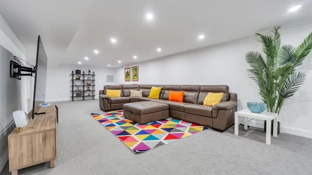 A bright living room with a sectional sofa, colorful rug, and potted palm.