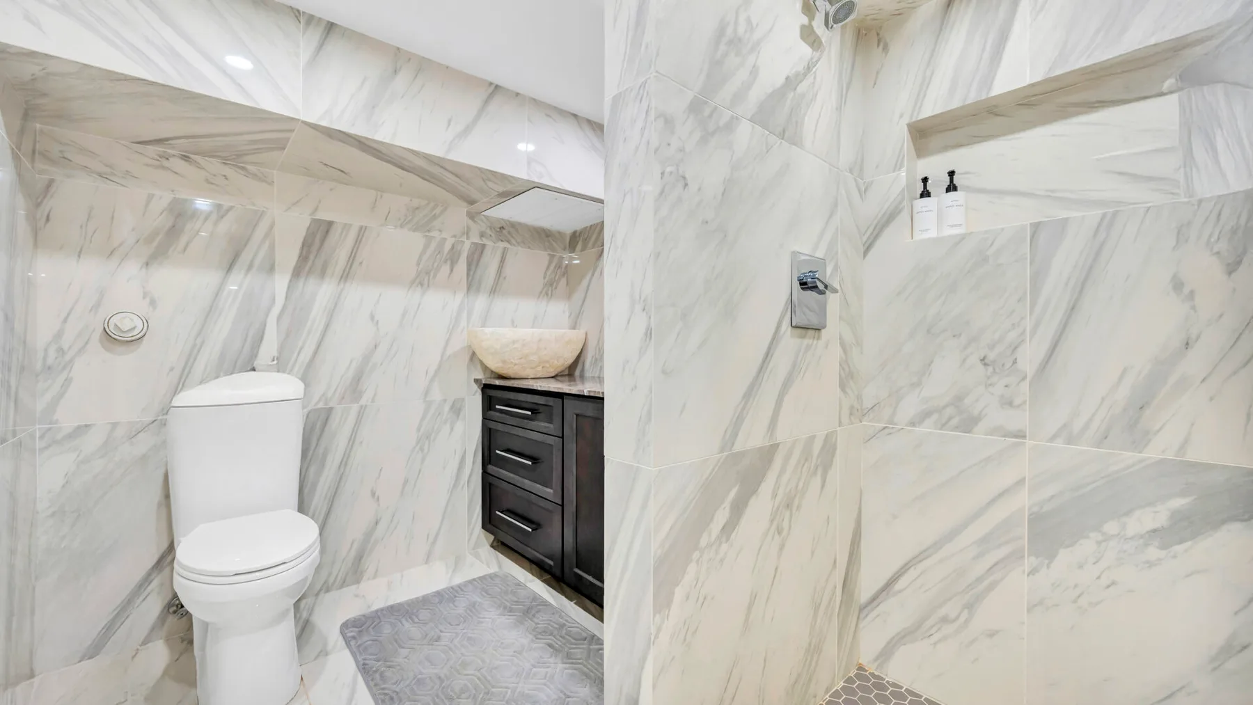 A marble-tiled bathroom with a toilet, vanity, and shower.