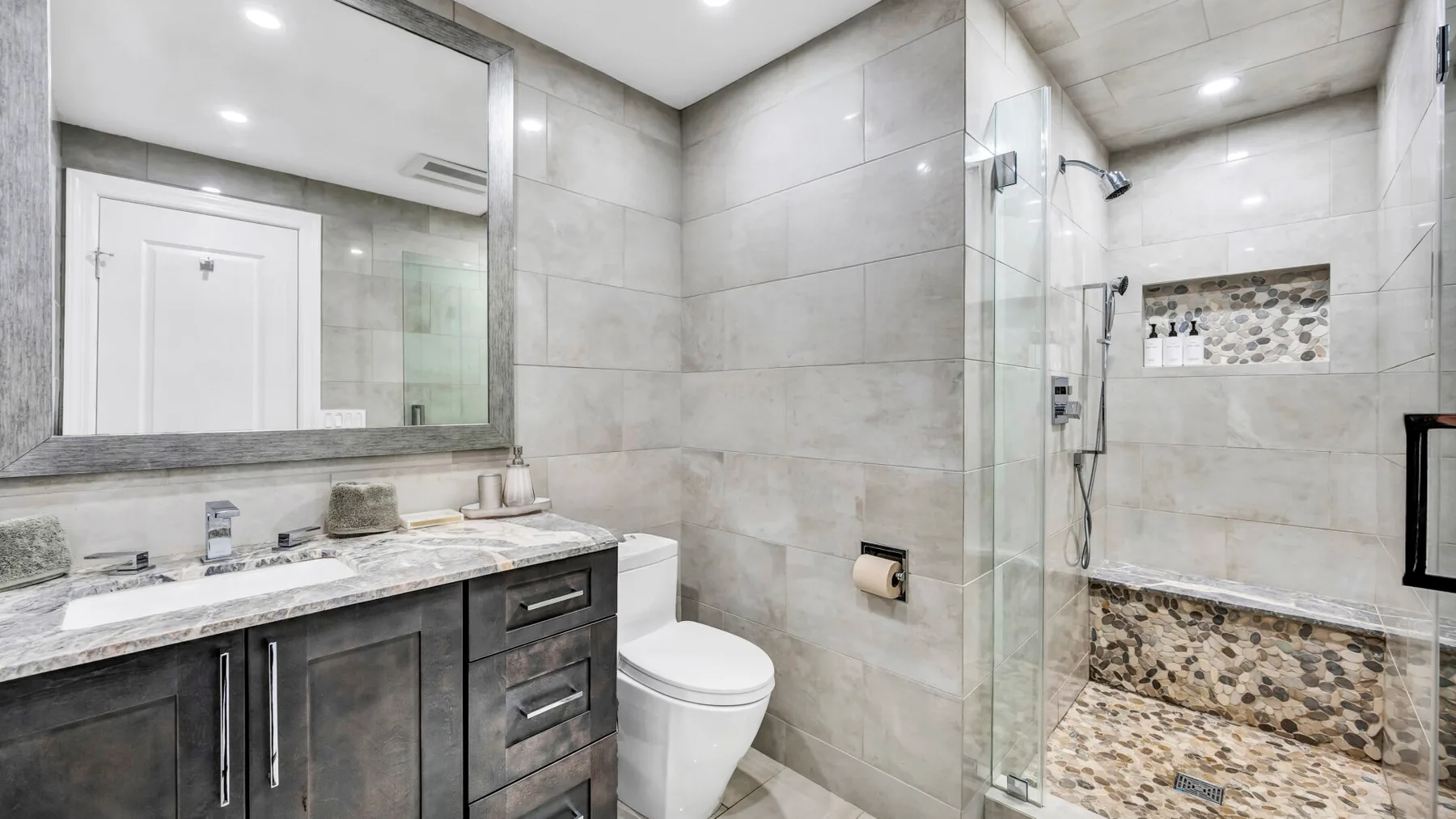 A tiled bathroom with a vanity, toilet, and glass shower.