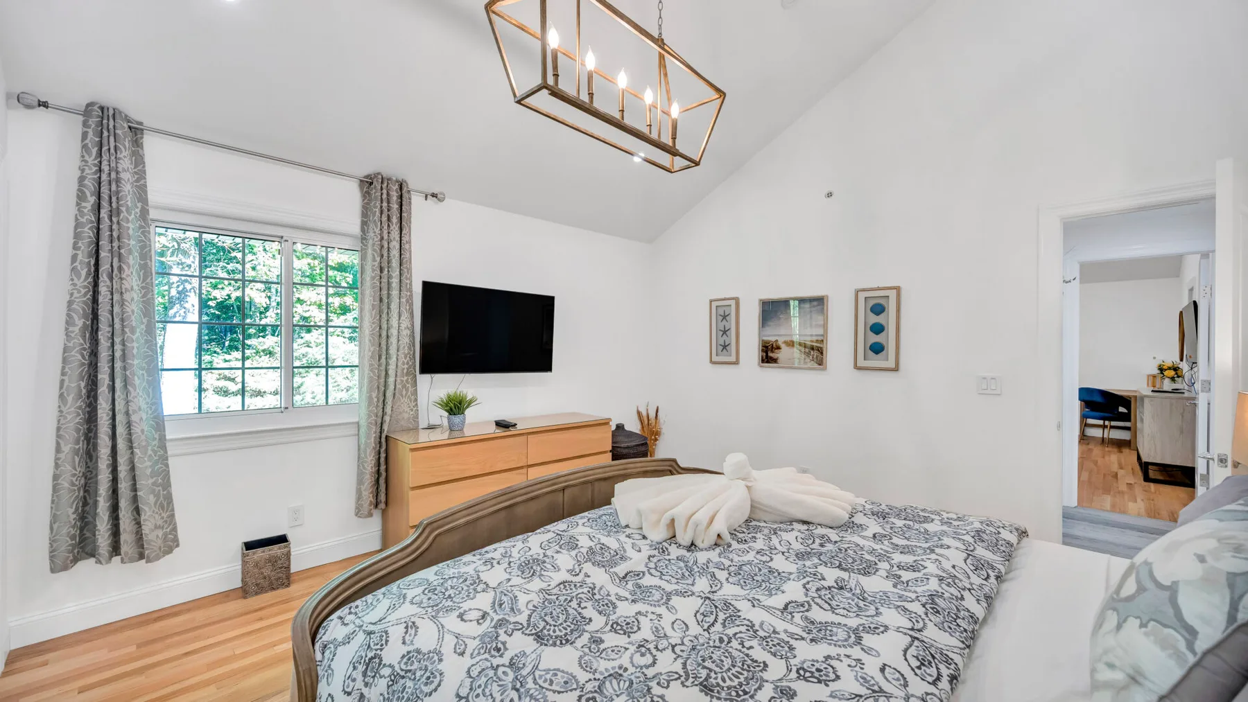 A bright bedroom with a patterned bed, a large window, and a wall-mounted television.