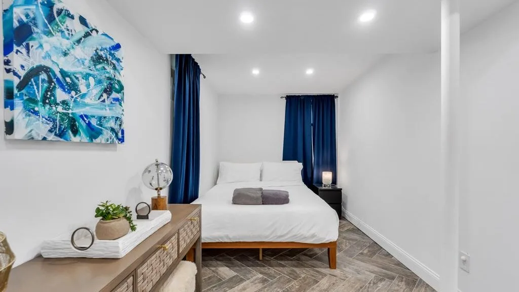 A bright bedroom with a neatly made bed and dark curtains.