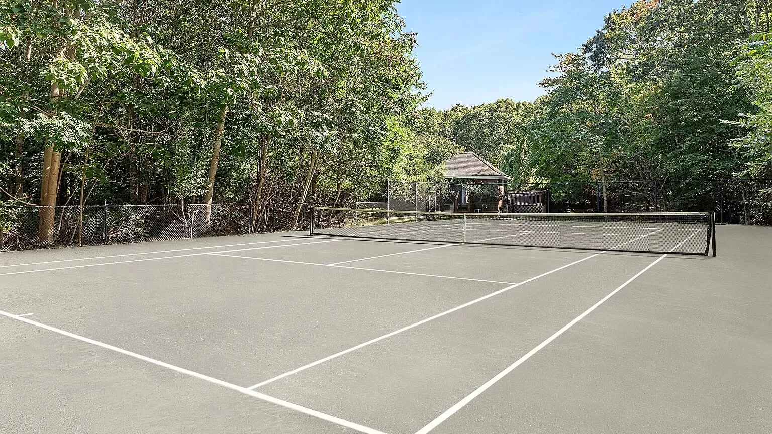 An outdoor tennis court is surrounded by trees, with a net across the court.