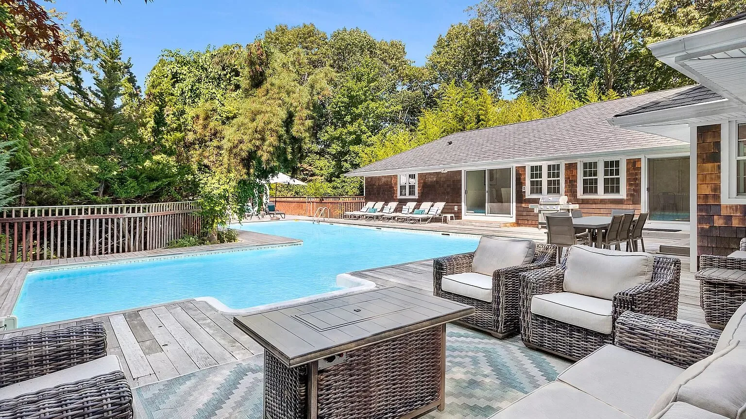 An outdoor swimming pool beside a furnished patio and trees.