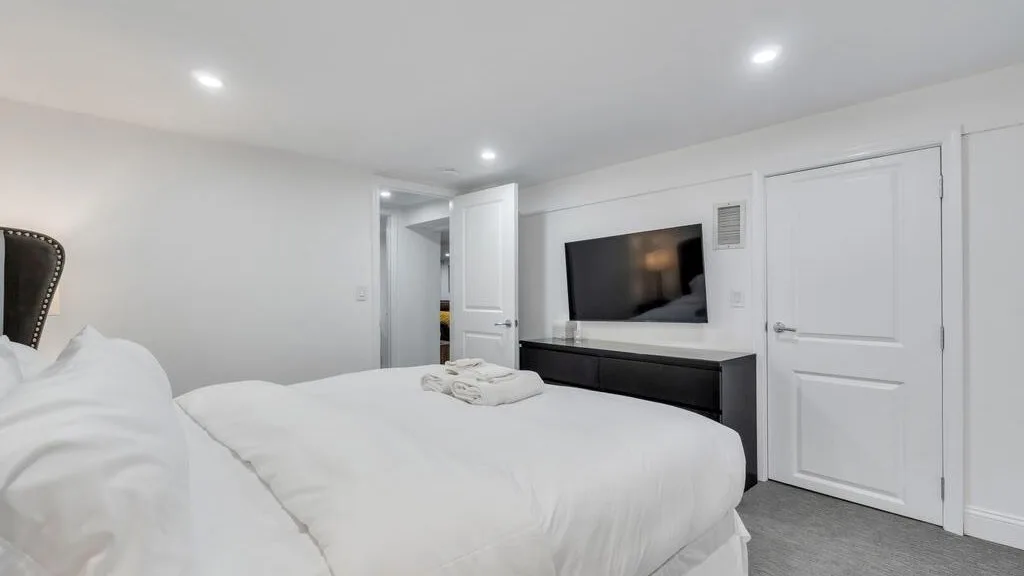 A bright bedroom with a neatly made bed and a wall-mounted television.