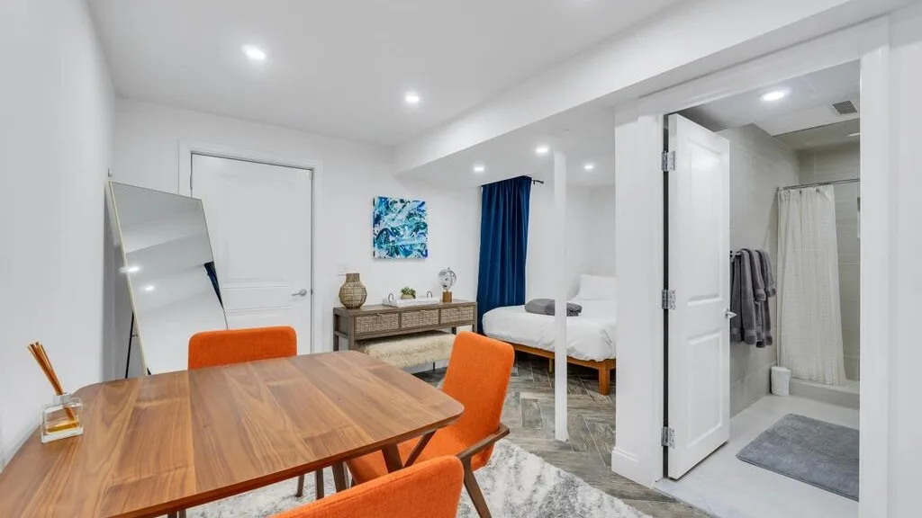 A bright dining area with a wooden table beside a bedroom and bathroom.