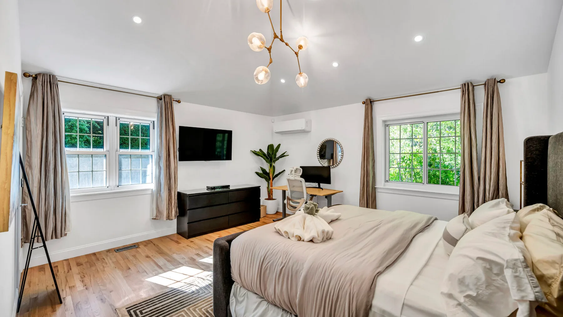 A bright bedroom with a large bed, windows, and a desk.