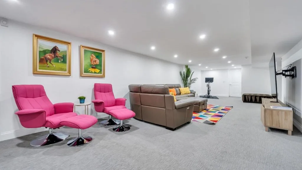 A spacious living room features pink seating, a brown sofa, and colorful wall art.