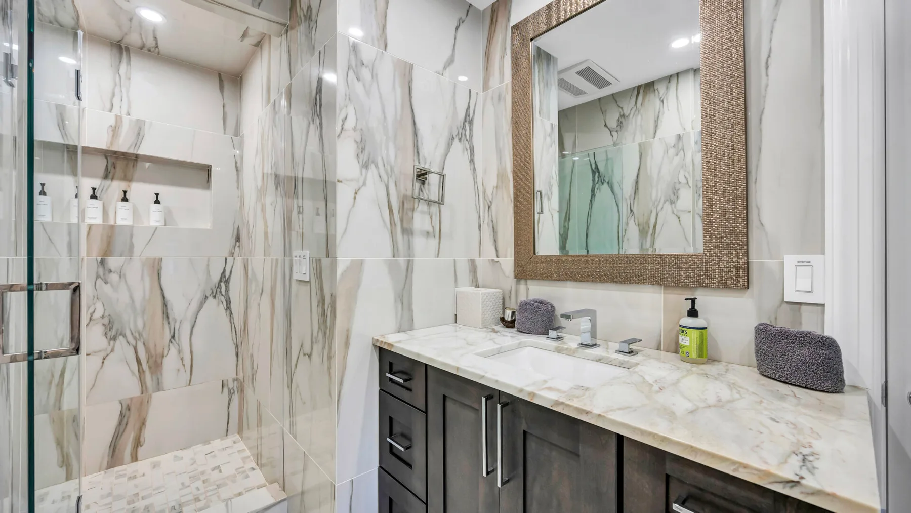 A marble-finished bathroom with a glass shower and a wide vanity.