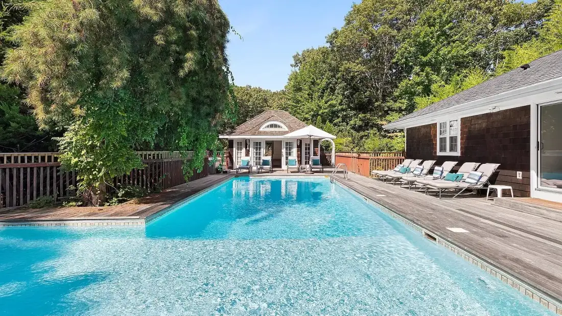 An outdoor swimming pool beside a house, with a deck and lounge seating.