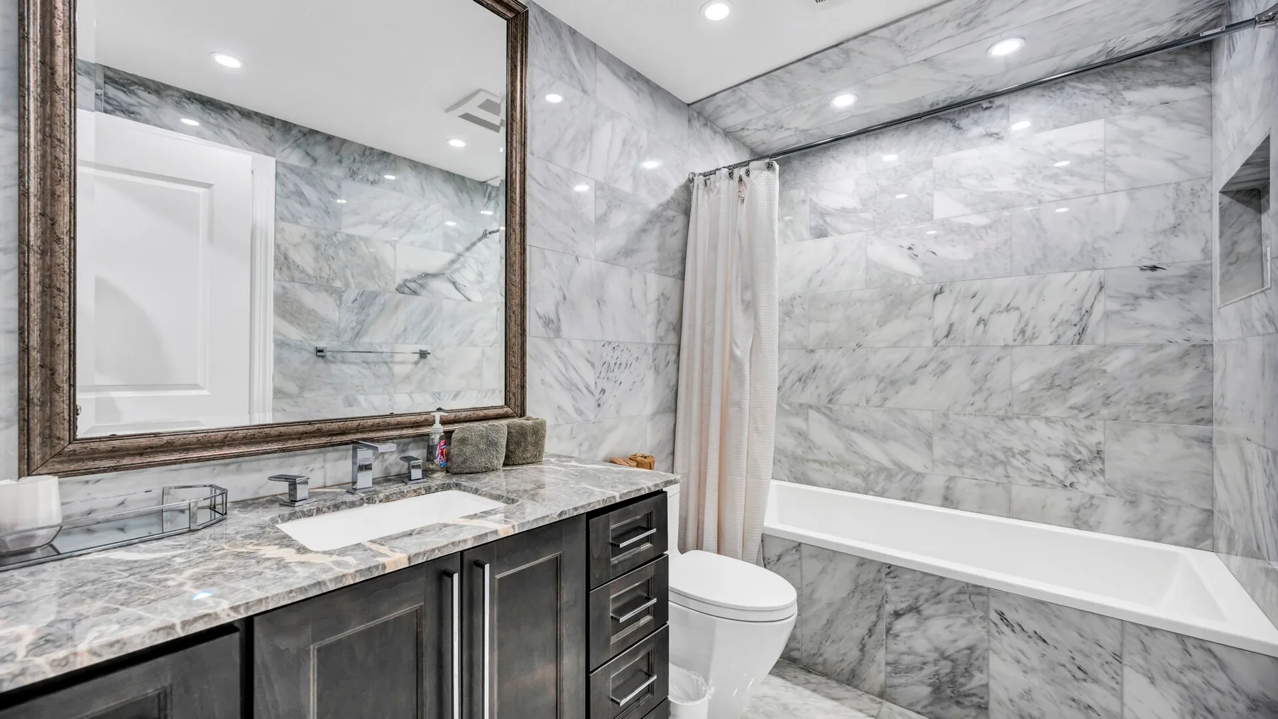 A marble bathroom with a vanity, toilet, and bathtub behind a shower curtain.
