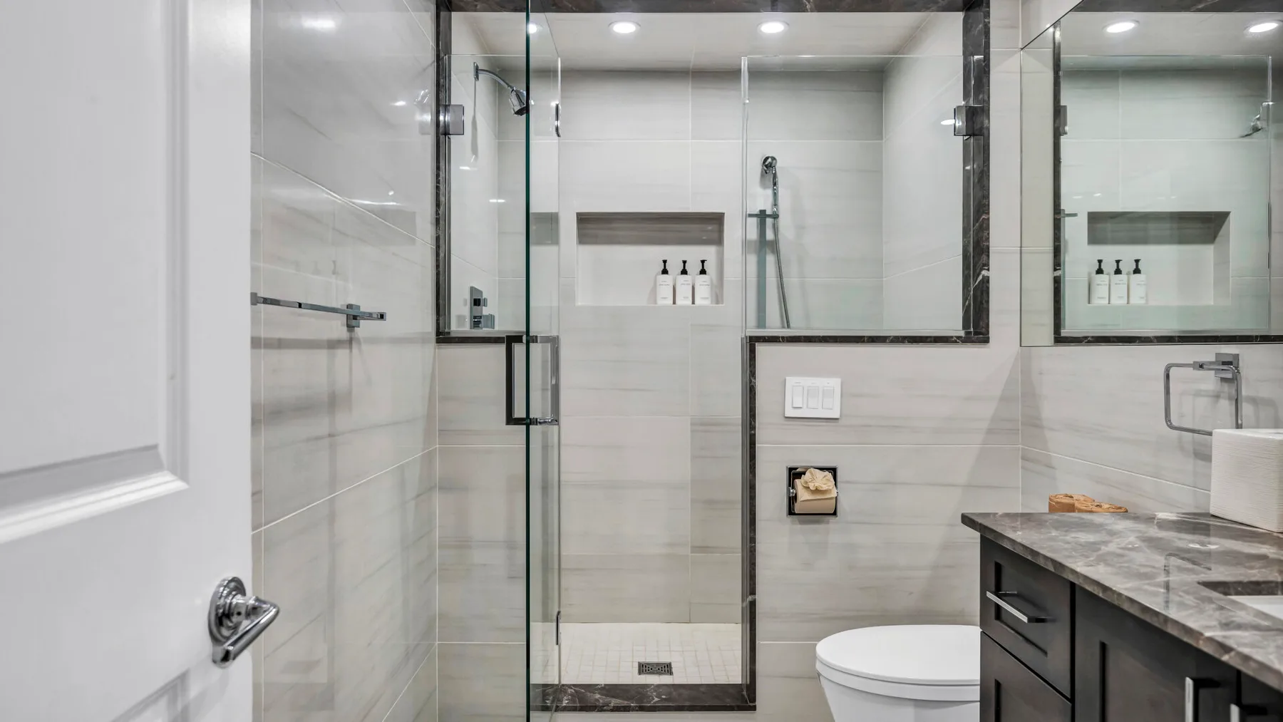 A tiled bathroom with a glass shower, toilet, and vanity.