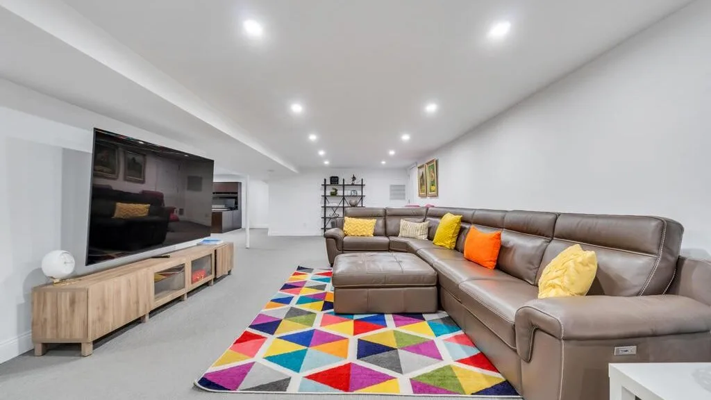 A living room with an L-shaped seating area, television, and colorful rug.