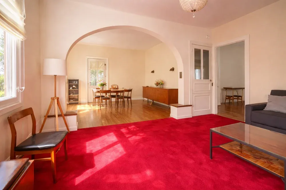 A living room with red carpet and an arched opening to a dining area.