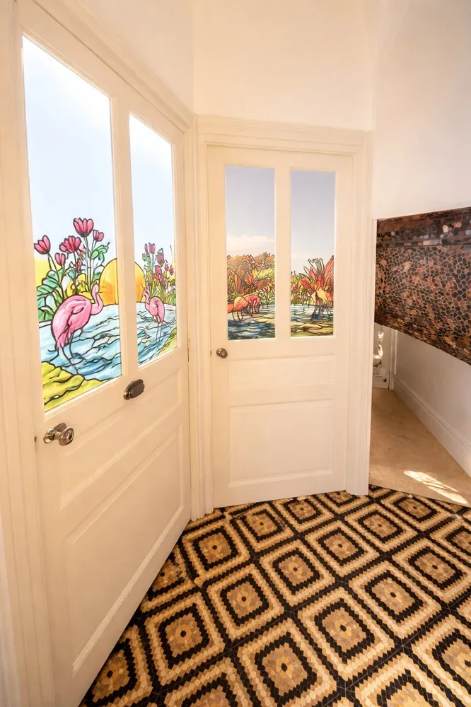 A bright hallway with white doors featuring colorful floral and flamingo artwork.