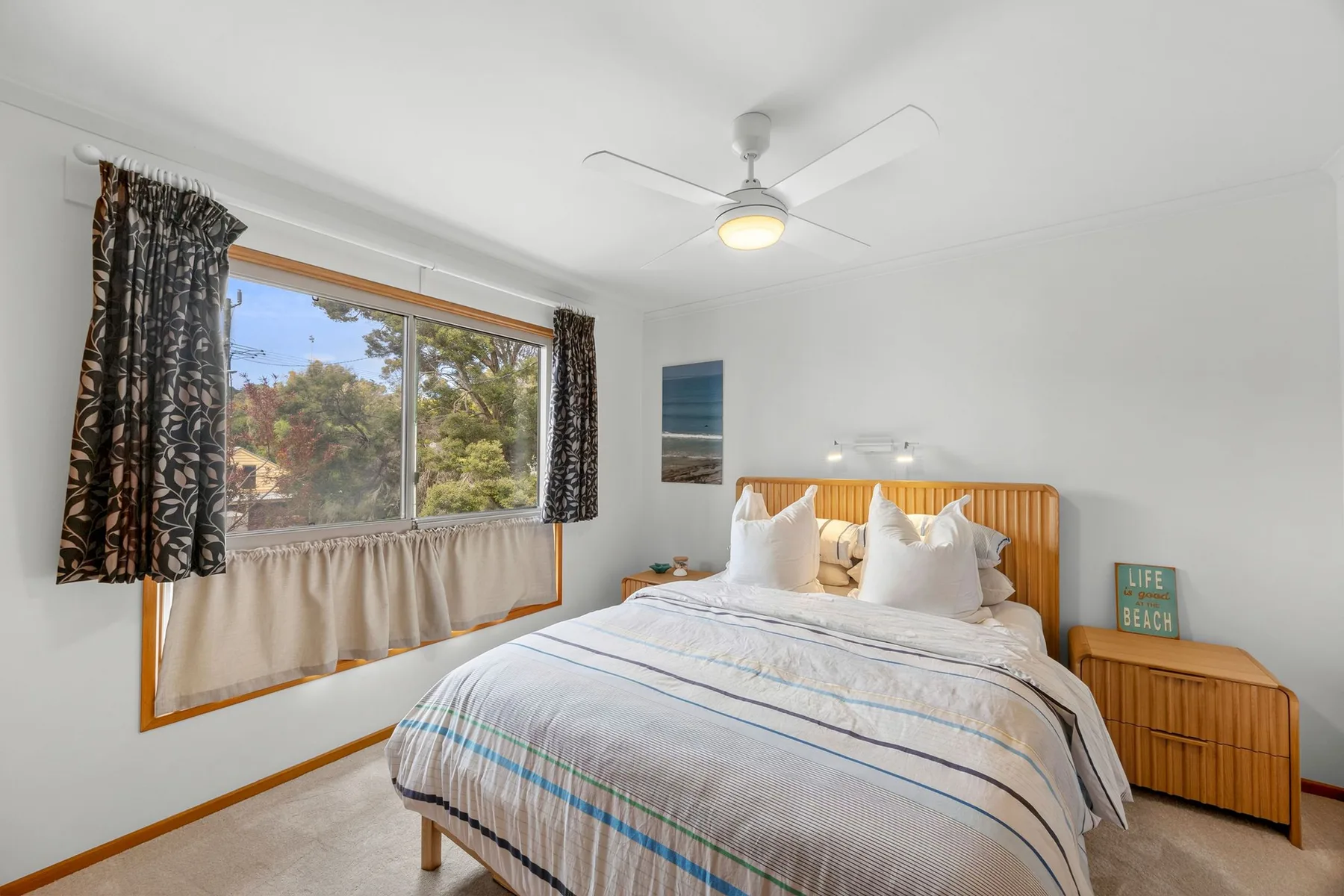 A bright bedroom with a bed beside a large window.