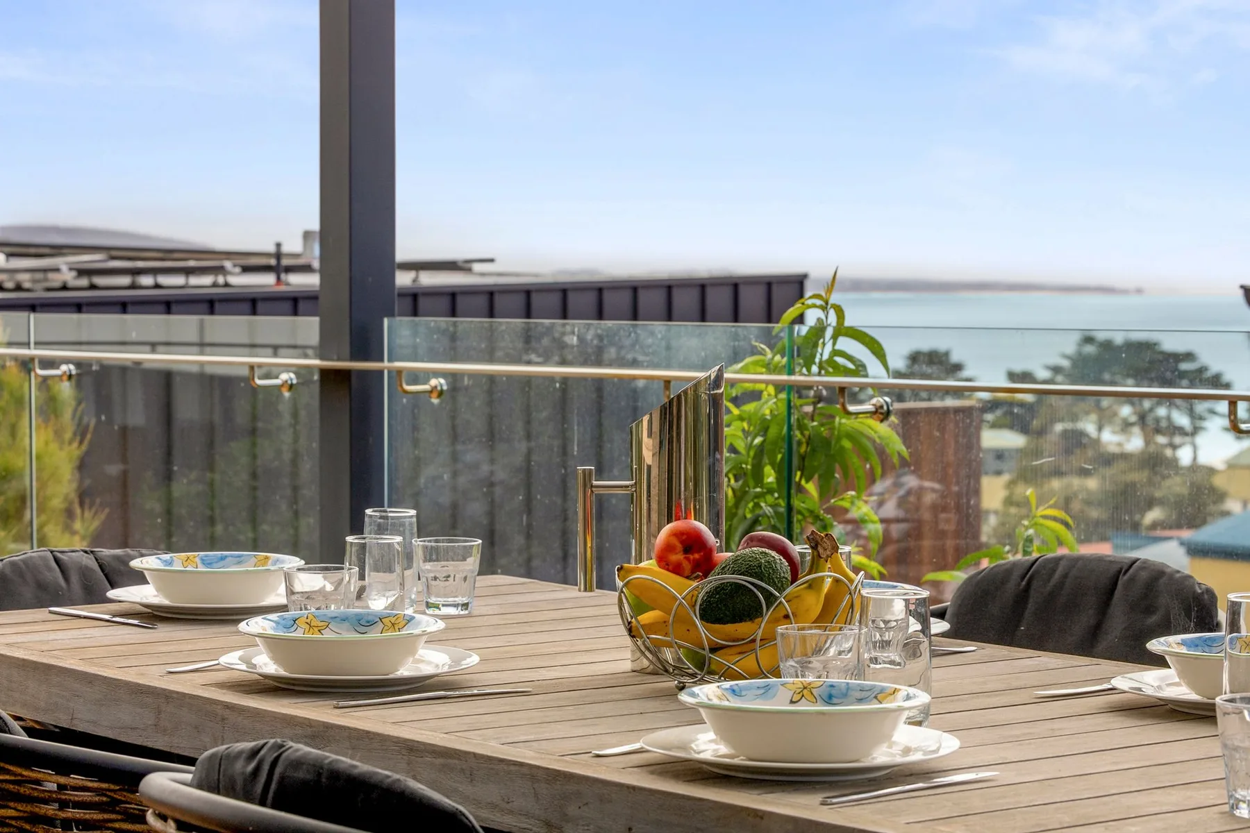 A dining table is set with dishes and fruit beside an outdoor terrace view.