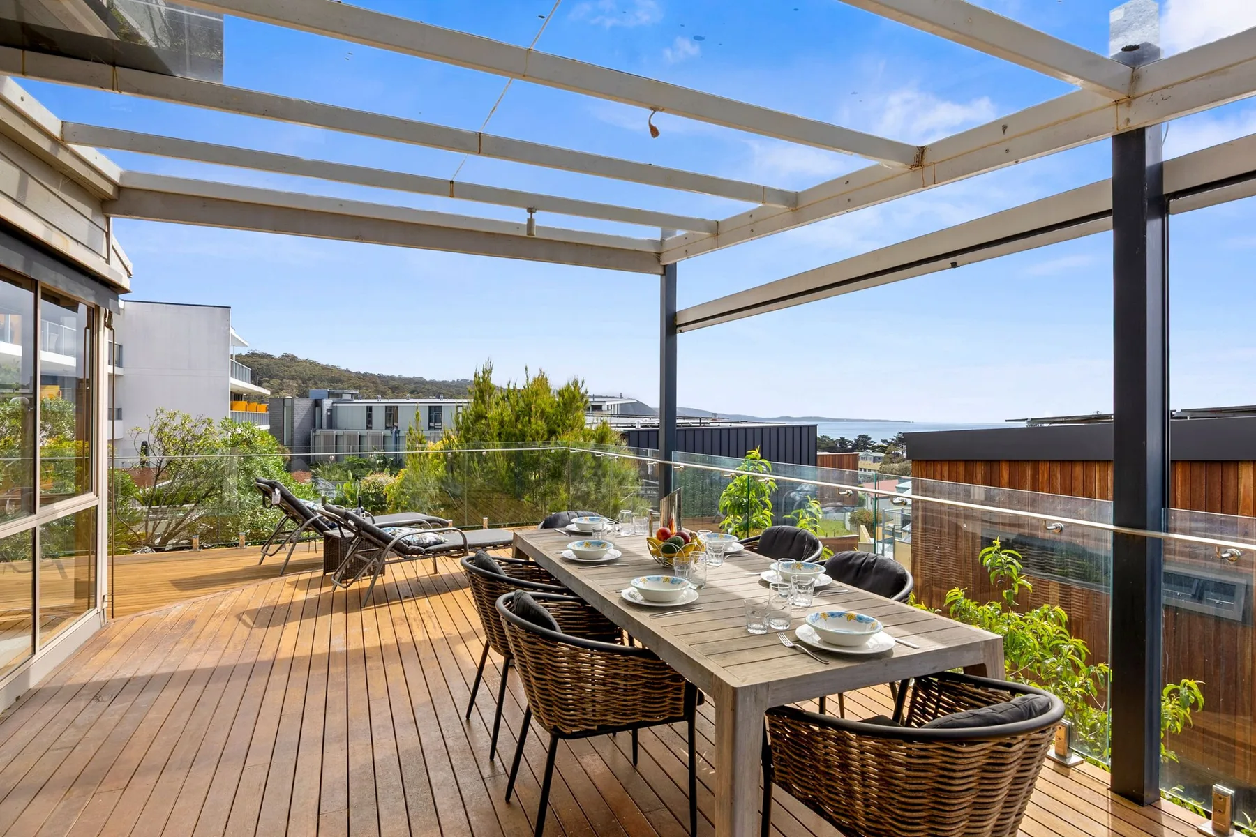 An outdoor dining area with a long table and seating beneath a pergola.