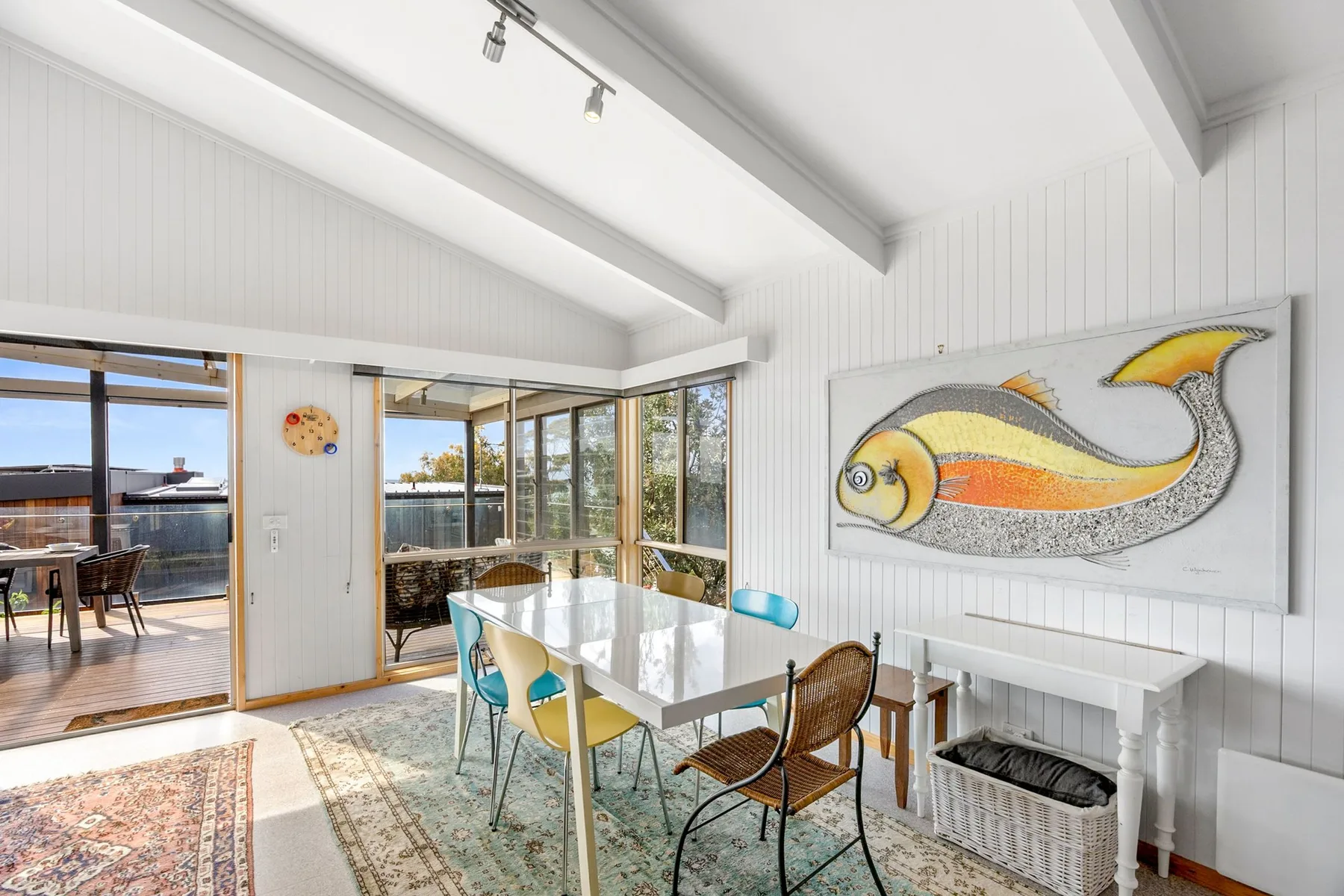A bright dining area with a glass table beside large windows opening onto a deck.
