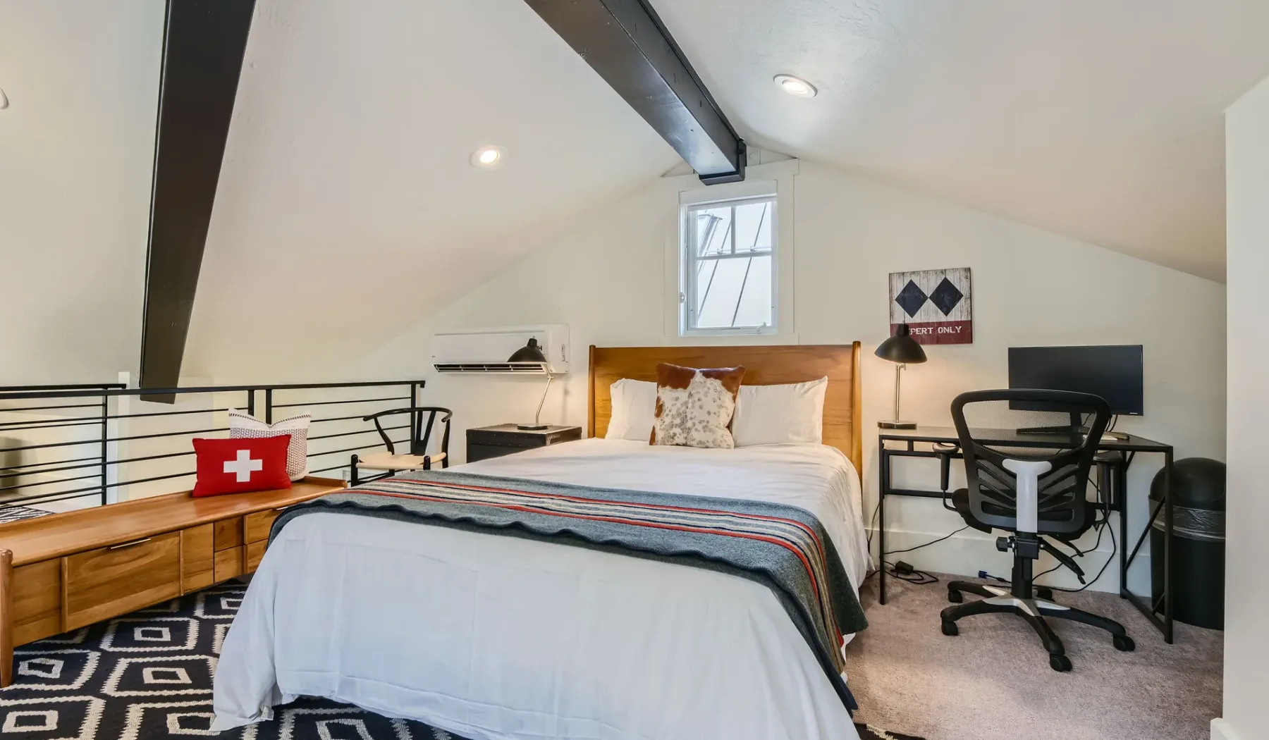 Un dormitorio con cama, escritorio y computadora bajo un techo inclinado.