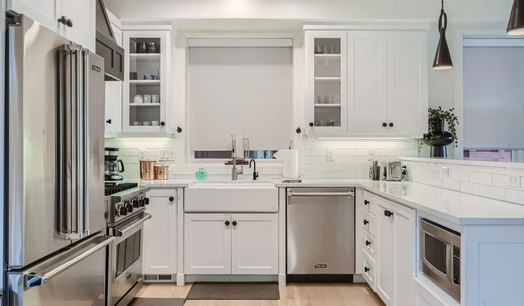 Una cocina blanca y luminosa con electrodomésticos de acero inoxidable y un fregadero central.