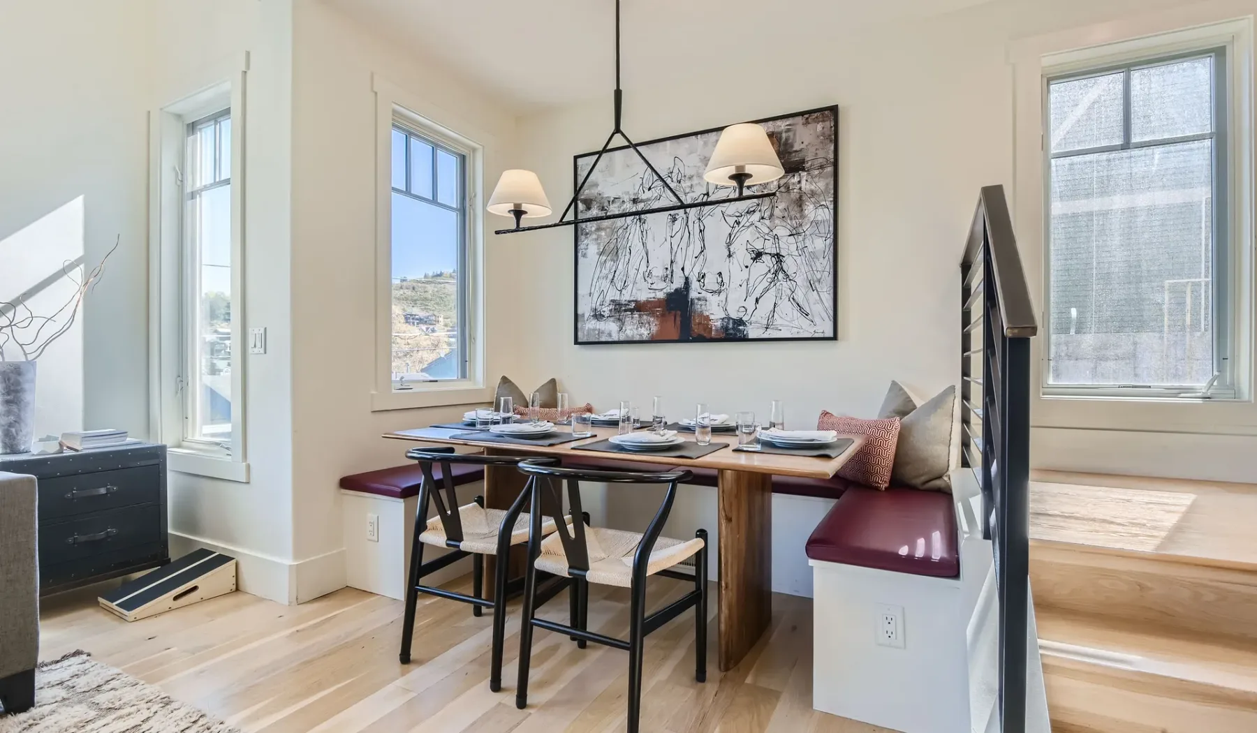 Un rincón de comedor con mesa de madera y banco empotrado bajo una lámpara colgante.
