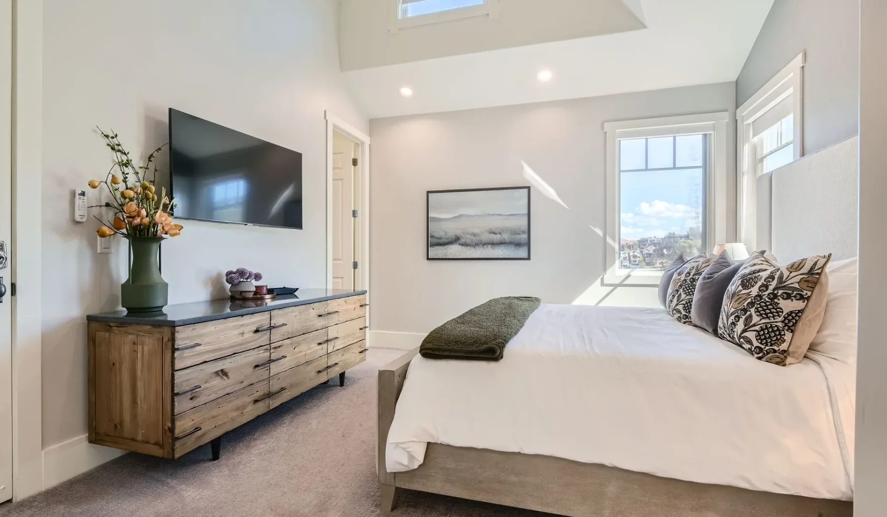 Un dormitorio luminoso con cama, cómoda y televisor en la pared.