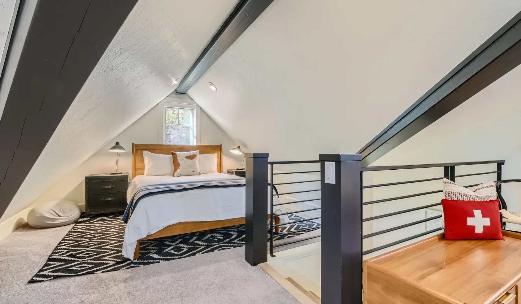 Un dormitorio tipo loft con una cama bajo un techo inclinado y una barandilla.