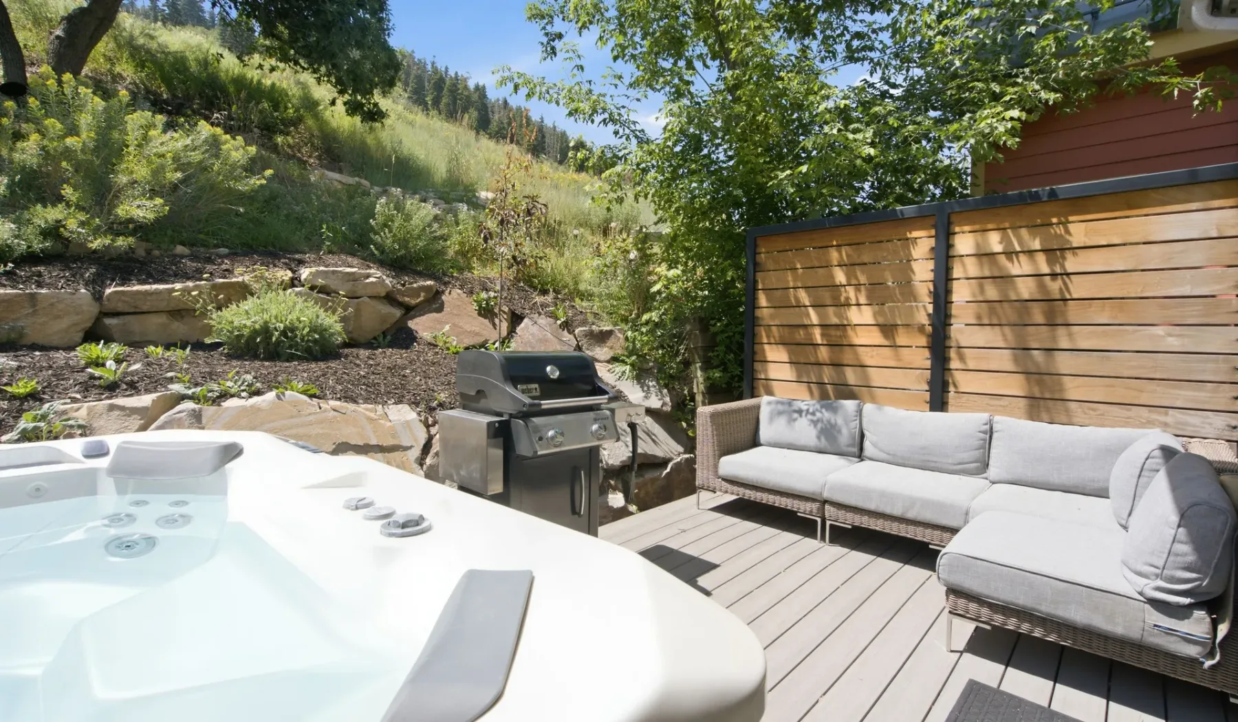 Una terraza exterior con jacuzzi, asientos acolchados y una parrilla.