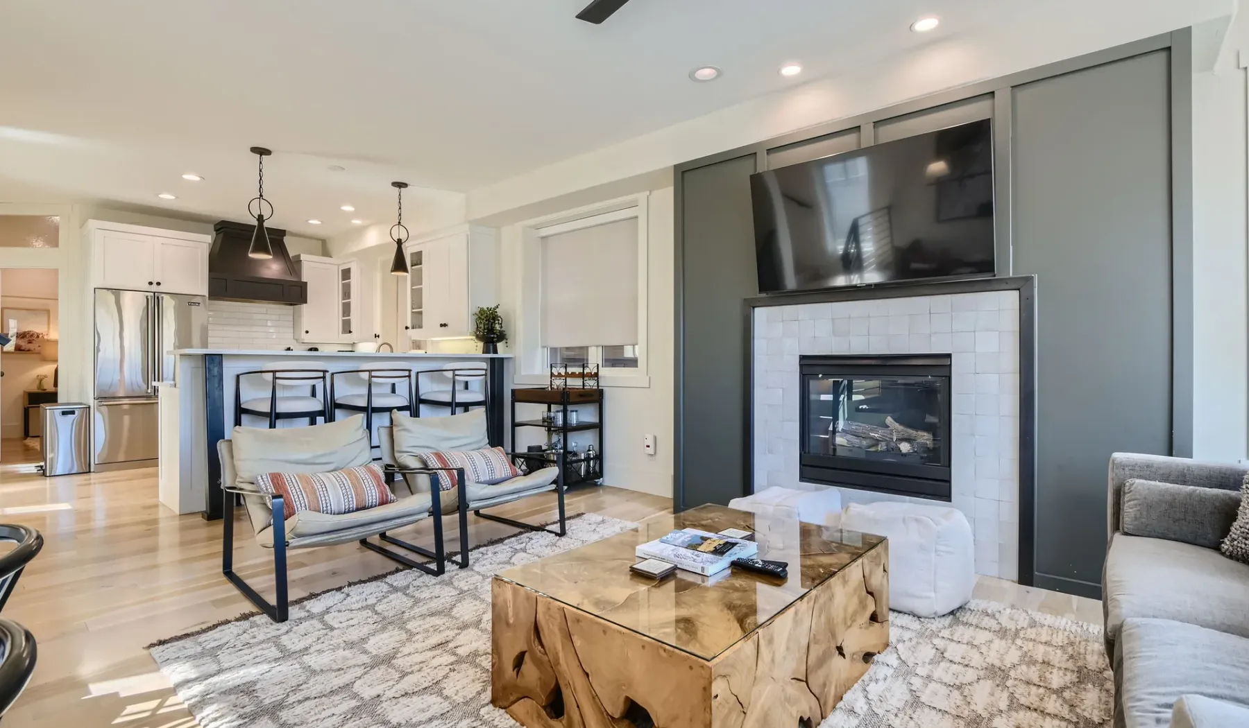 Una sala de estar con chimenea, televisor y asientos junto a una cocina abierta.
