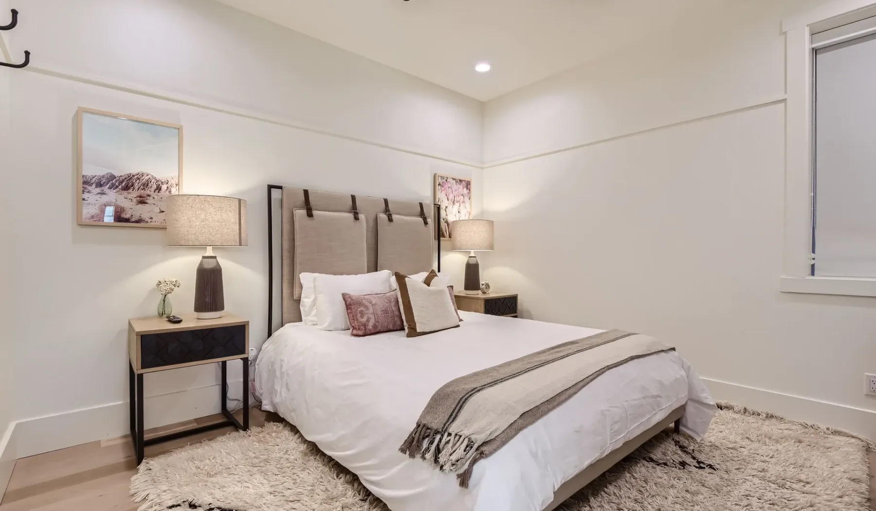 Un dormitorio luminoso con una cama bien tendida, mesitas de noche y cuadros enmarcados.