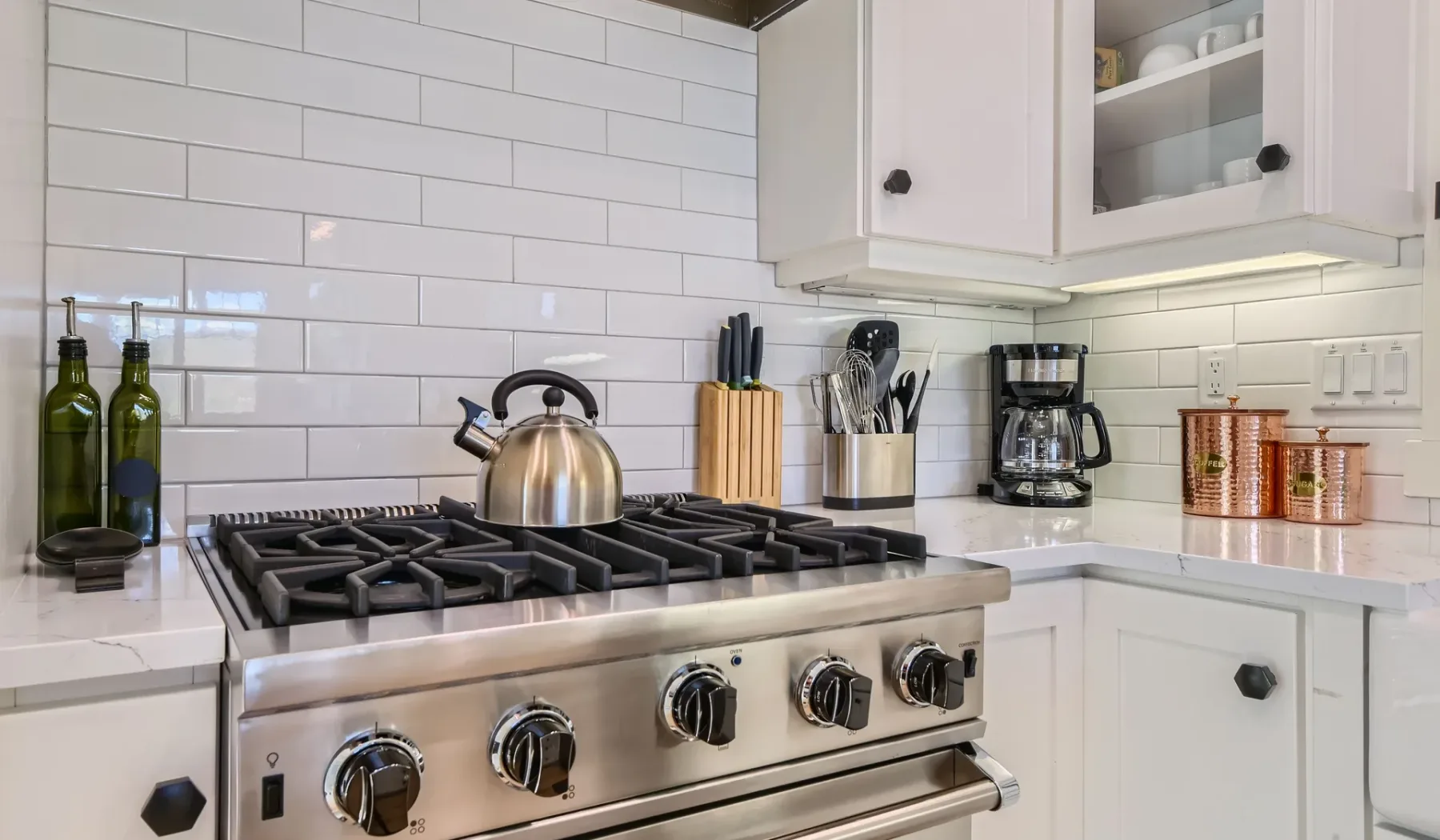 Una cocina con una estufa de acero inoxidable bajo paredes de azulejos blancos.