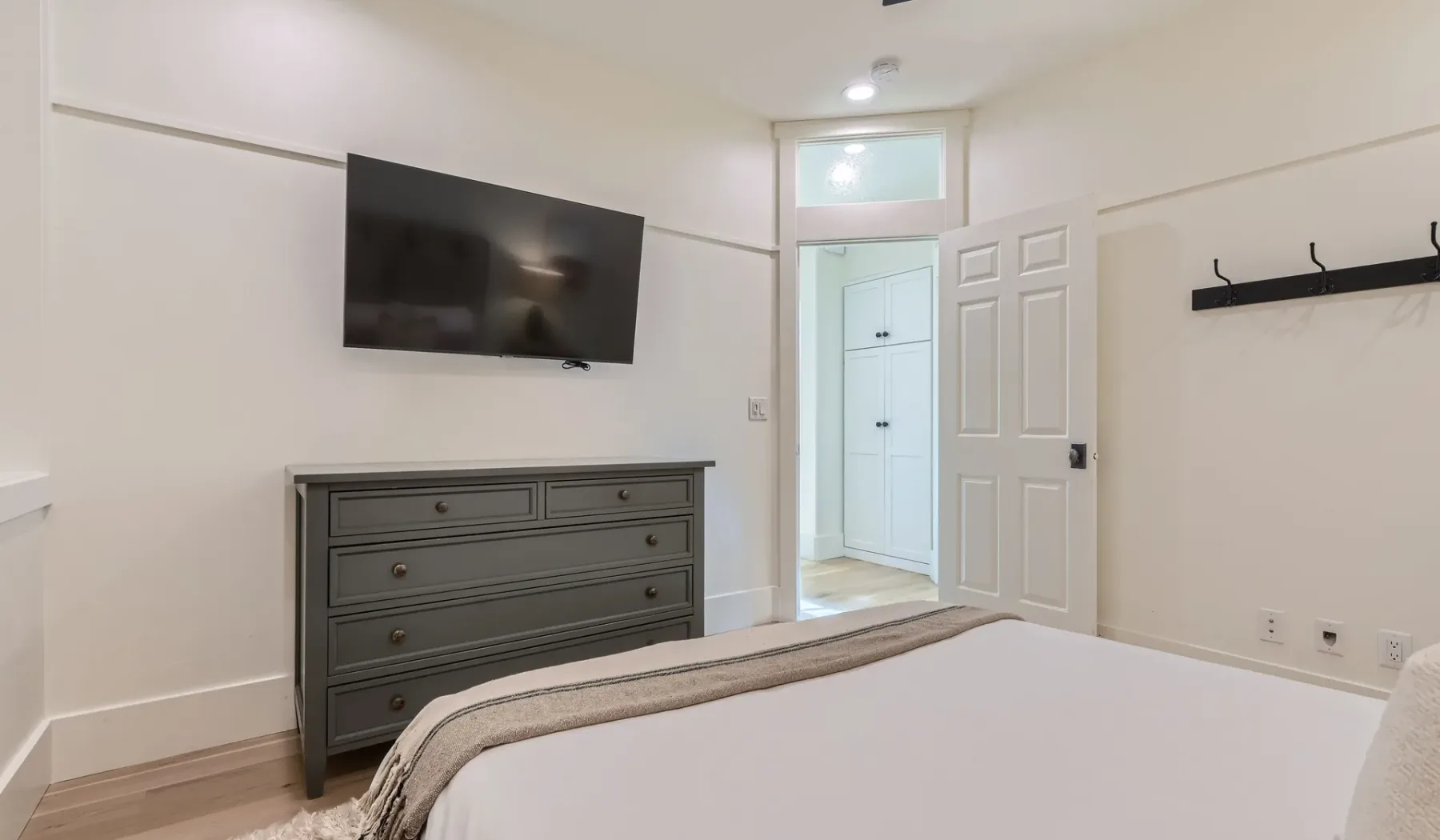 Un dormitorio con cama, cómoda y televisor montado en la pared.
