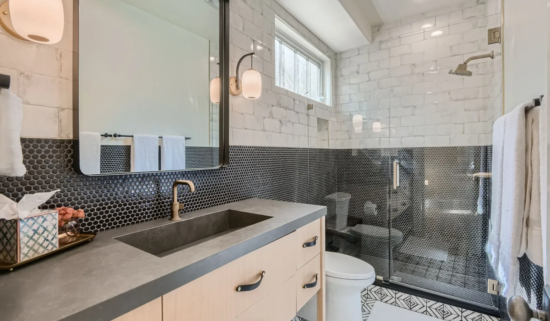 Un baño con un mueble de lavabo largo, inodoro y ducha de vidrio.