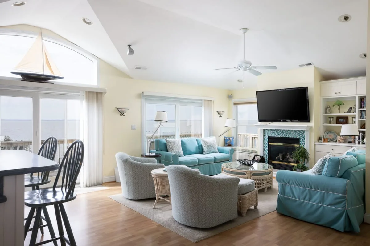 A bright living room with teal seating, a television, and large windows.