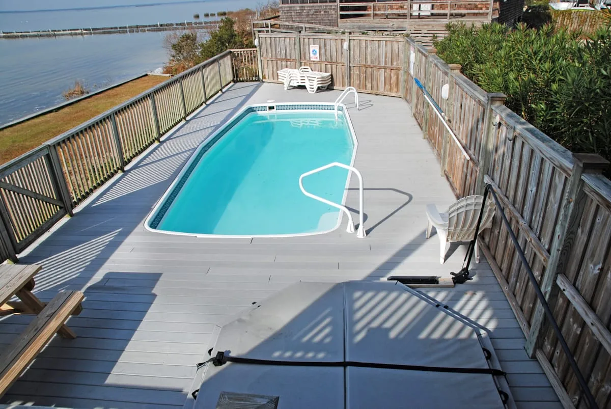 Una piscina al aire libre está en una terraza de madera junto al agua.