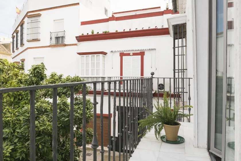 A small balcony with dark metal railings overlooks a white building with red trim.