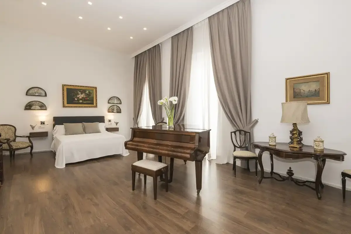 A bedroom with a grand piano beside tall curtained windows.