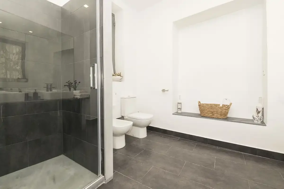 A bathroom with a shower, toilet, and a basket on the window ledge.