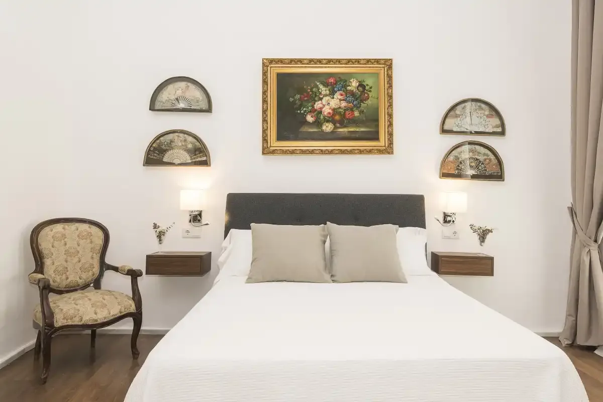 A bedroom with a neatly made bed and framed floral artwork above the headboard.