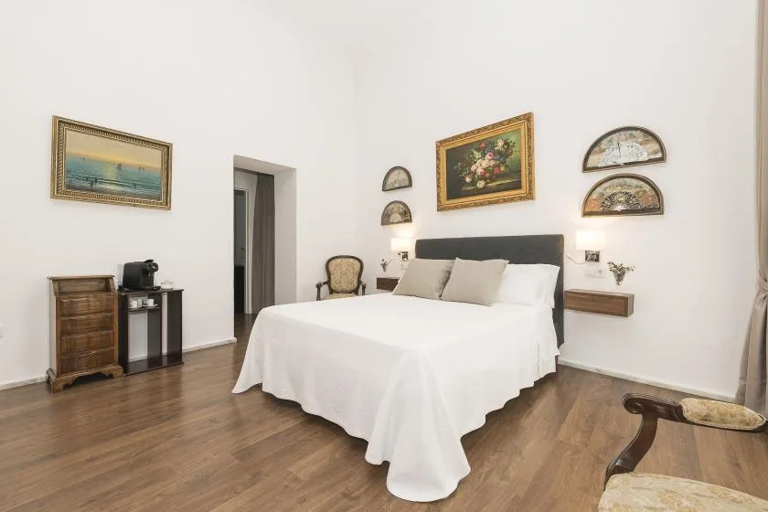 A bedroom with a neatly made bed, framed artwork, and wood flooring.