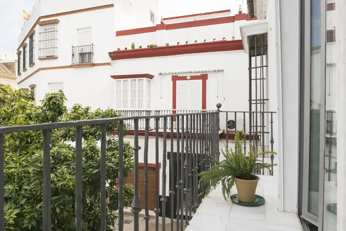 A balcony overlooks a white building with red trim and leafy plants.