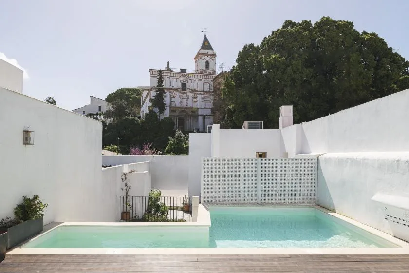 A small outdoor pool sits among white walls, with a historic building visible beyond.