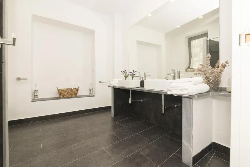 A bright bathroom with a long vanity, sink, and folded towels.