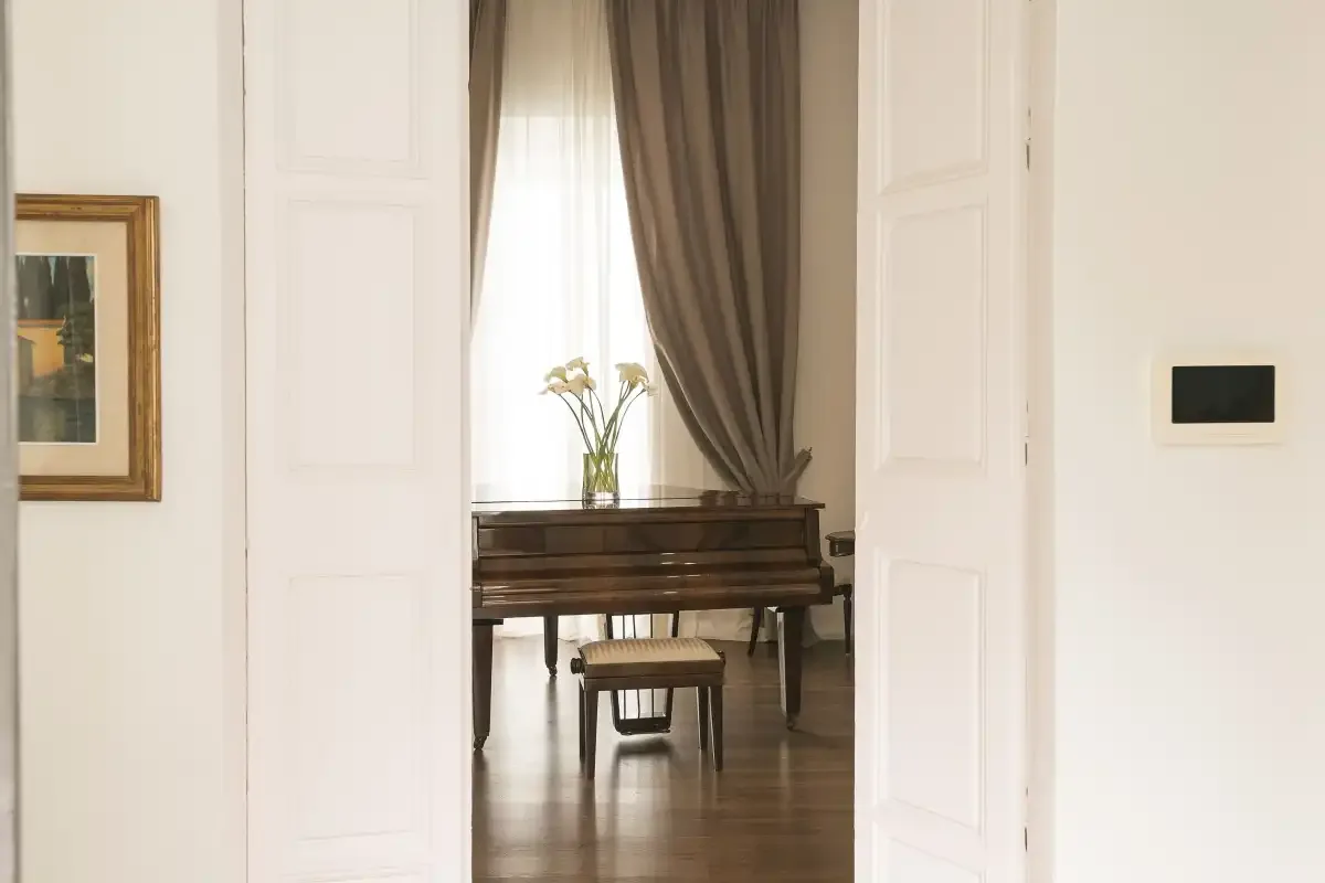 A piano sits by a curtained window in a bright interior.