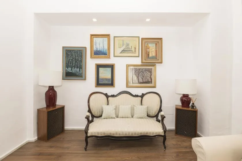A decorative settee sits beneath a gallery of framed artwork in a bright room.