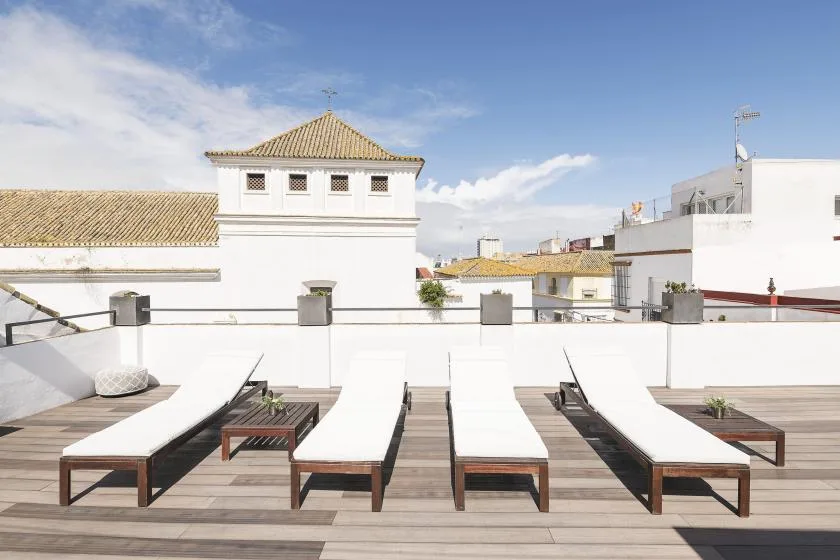 A rooftop terrace with rows of lounge seating and white buildings in the background.
