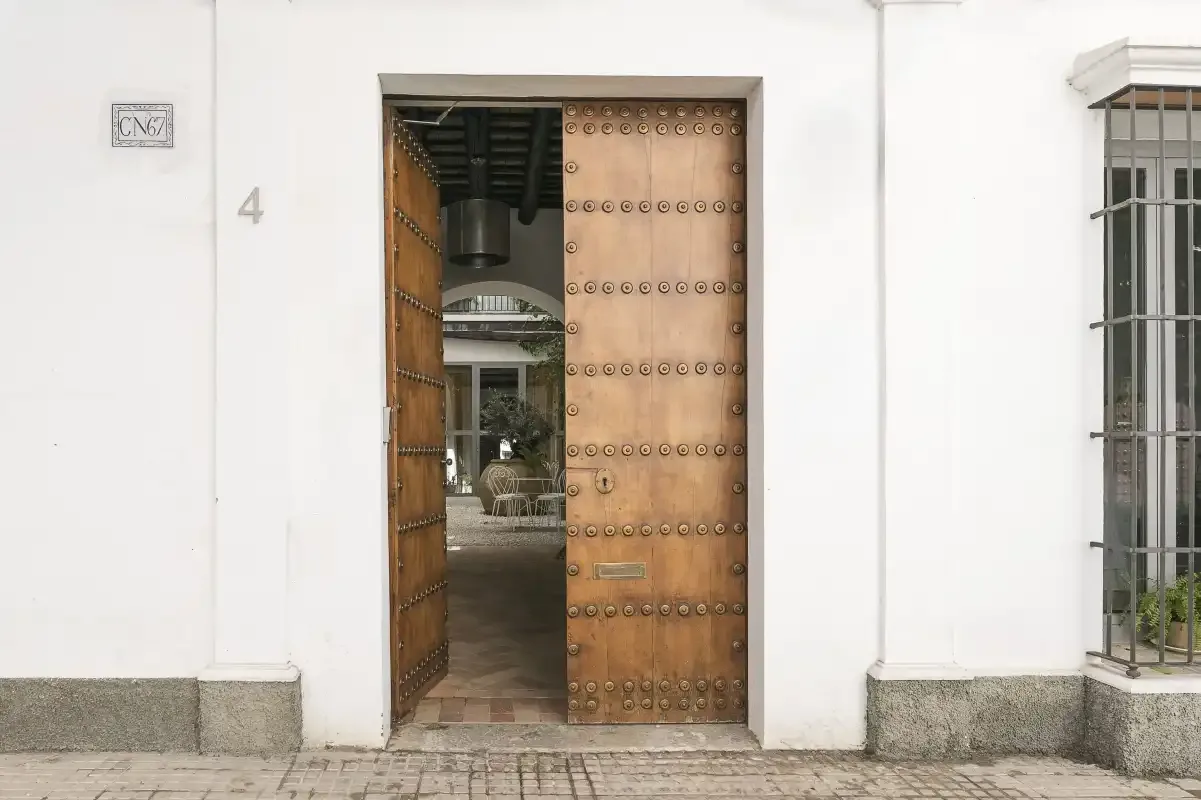 A large wooden entrance door stands open in a white exterior wall.