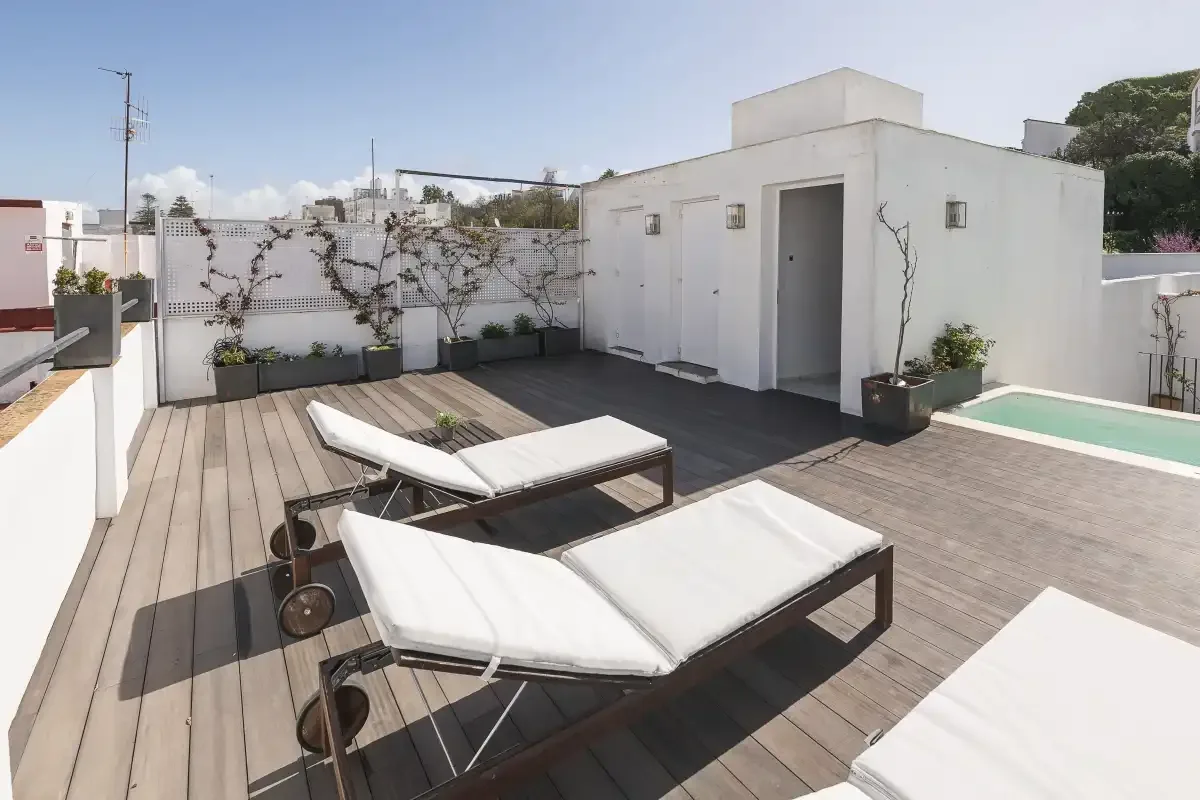 A rooftop terrace with cushioned lounge chairs and potted plants.