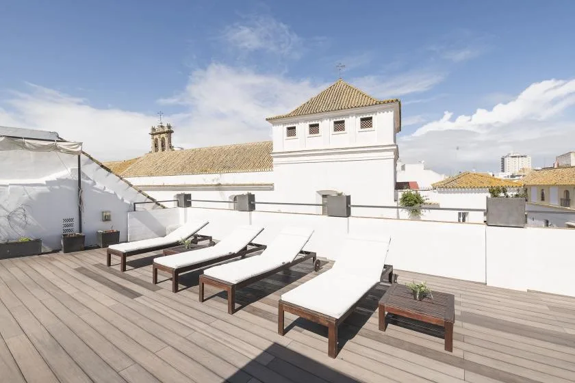A rooftop terrace with lounge seating and white walls under a blue sky.